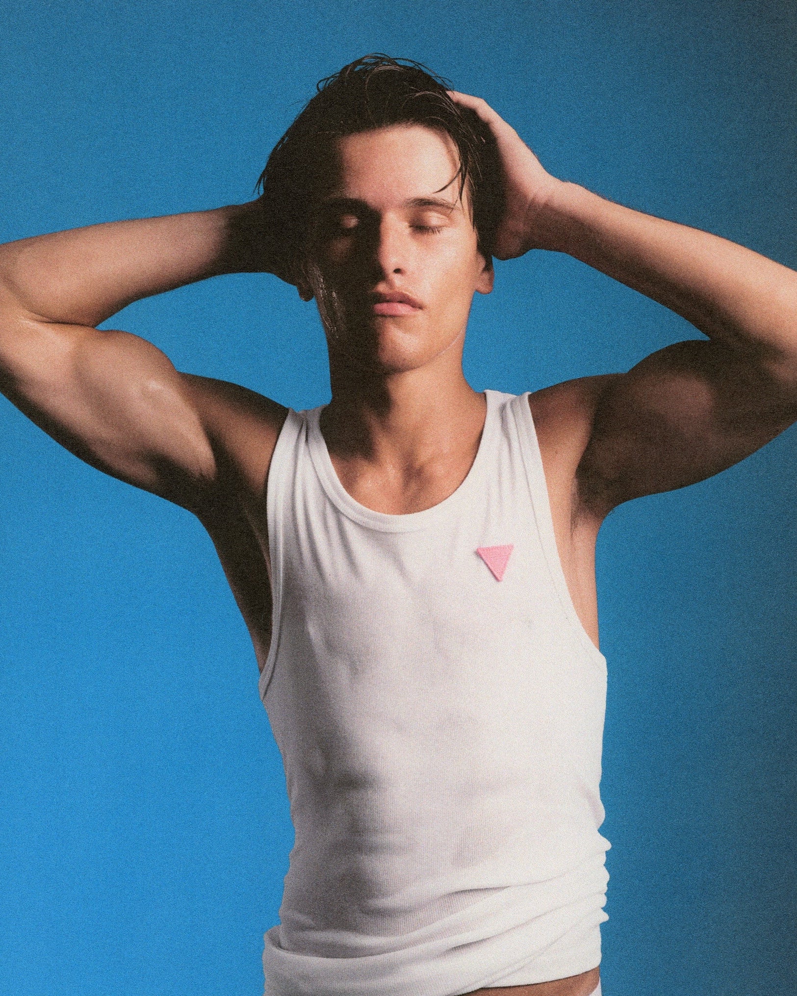 Man wearing a white tank top with a pink triangle logo against a blue background